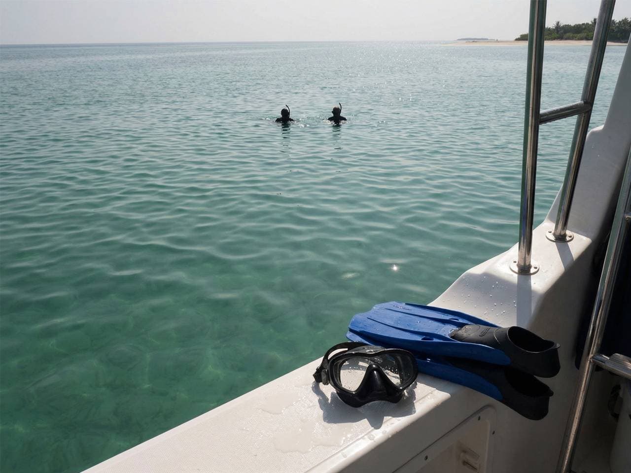 Snorkel mask and fins resting on the boat with snorkelers in the water